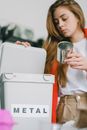 Low angle of serious female with long hair putting tin can into opened bucket for metal trash
