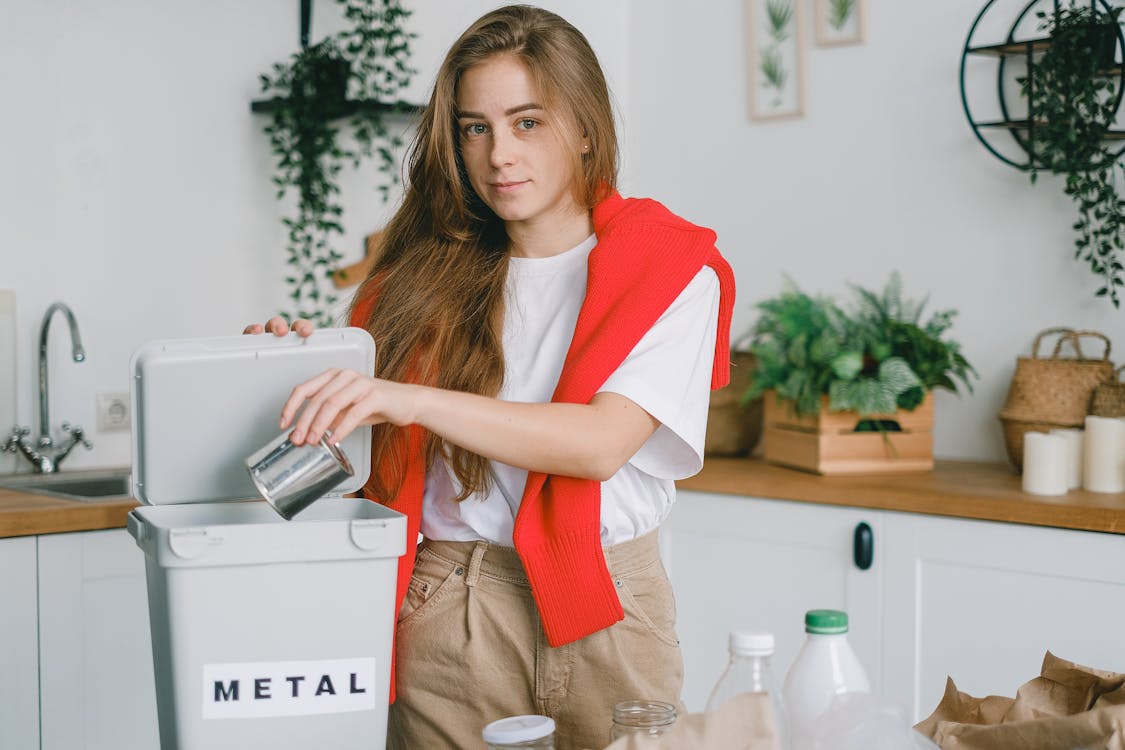 Responsible female sorting garbage while putting tin can into container for metal litter and looking at camera