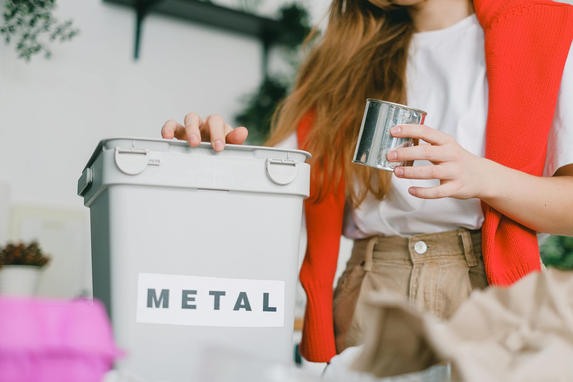 Low angle of female putting tin can into bucket for metal trash for recycling litter