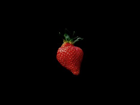 Close-up of a single fresh strawberry against a black backdrop.