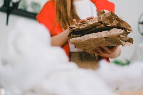 Low angle of crop anonymous female standing with heap of crumple paper while separating trash for recycling