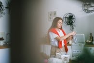 Young woman looking away while standing near table with rubbish in kitchen and collecting glass into special bucket