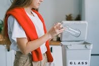 Crop anonymous female in casual clothes utilizing empty glass bottle into rubbish bin while cleaning kitchen and sorting out rubbish at home