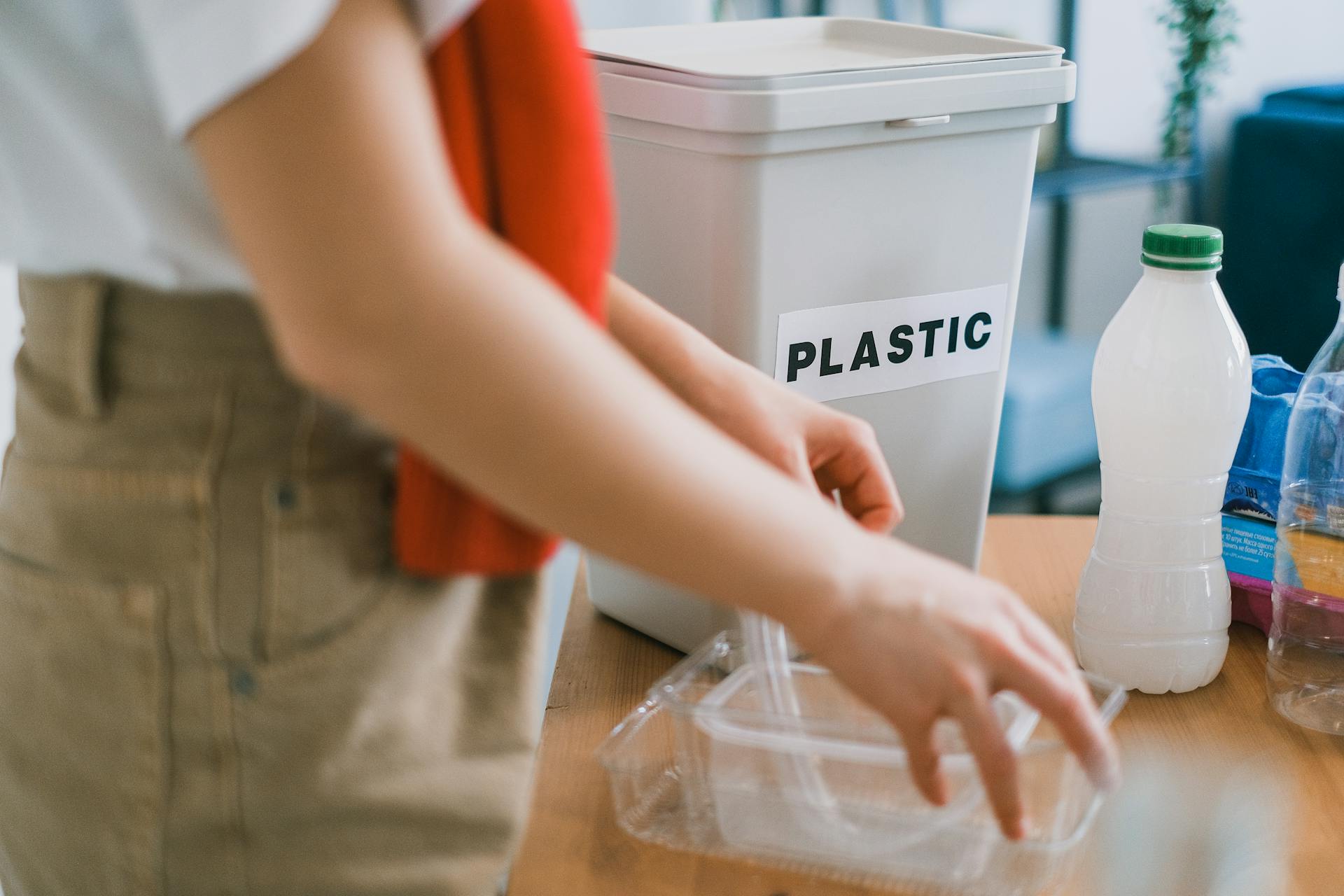 Crop anonymous female in casual clothes standing near bucket for plastic and sorting out rubbish in light room