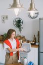 Young woman in casual clothes standing near table and throwing plastic into special bucket in daytime in kitchen