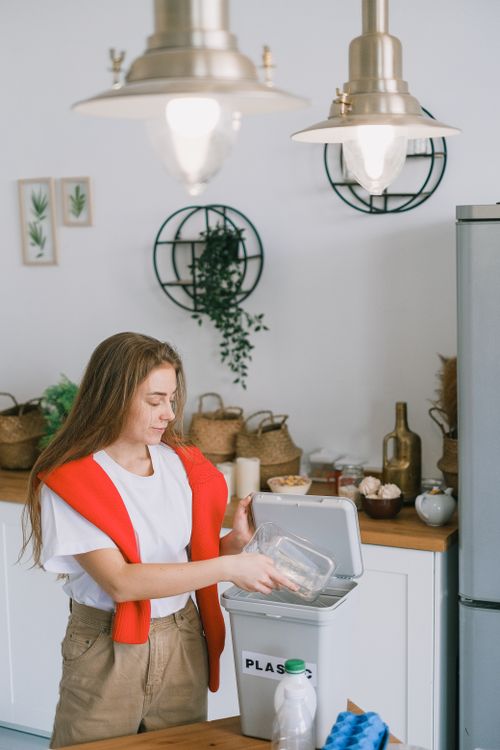 Free Young woman in casual clothes standing near table and throwing plastic into special bucket in daytime in kitchen Stock Photo