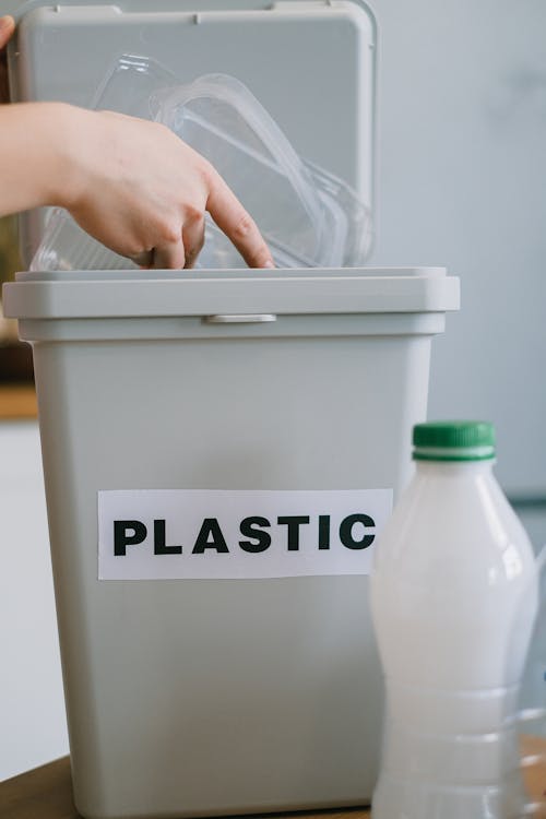 Crop anonymous person collecting plastic rubbish into bucket while cleaning home in daytime