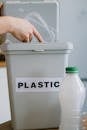 Crop anonymous person collecting plastic rubbish into bucket while cleaning home in daytime