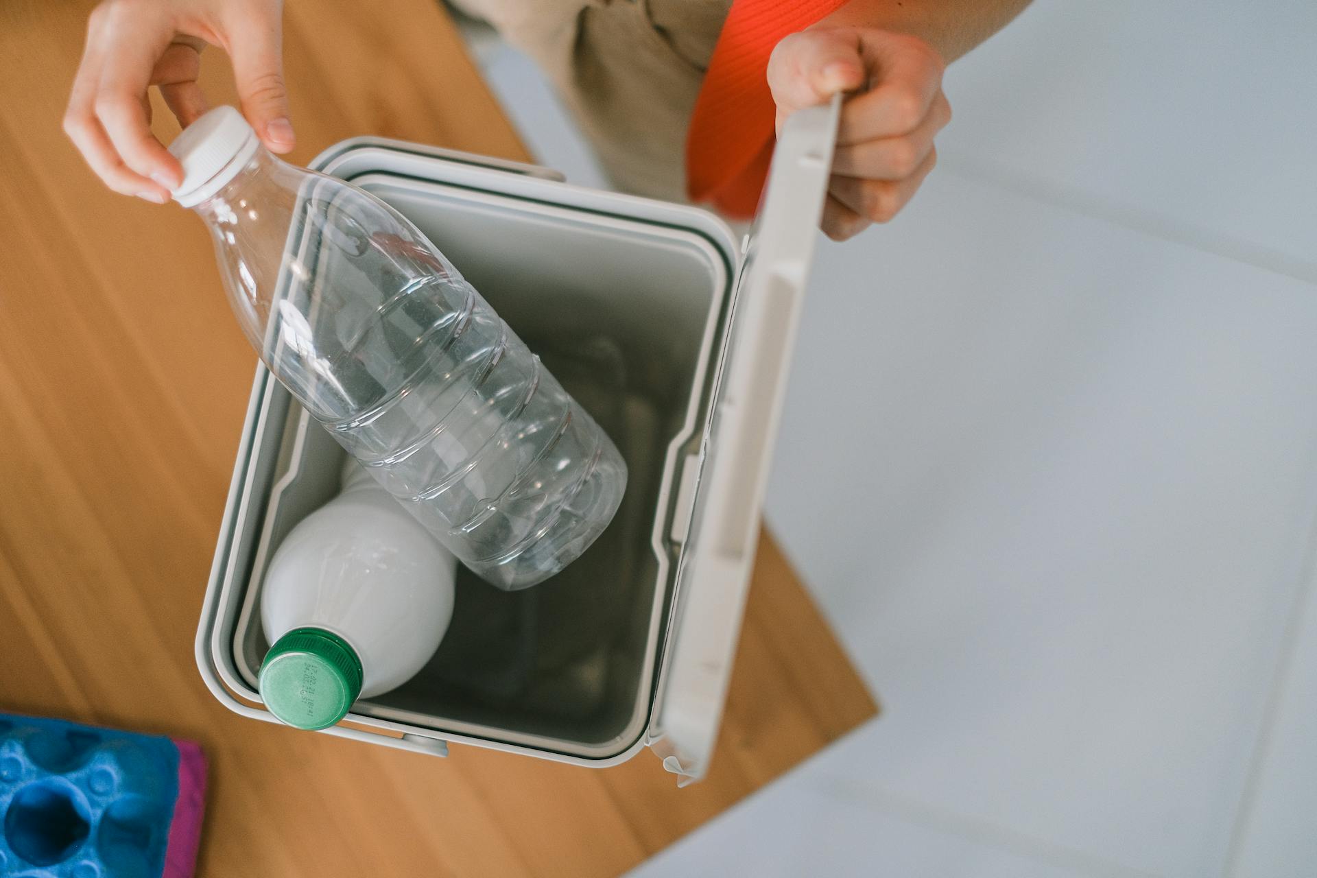 Top view of crop anonymous person opening container while disposing plastics bottle on wooden table