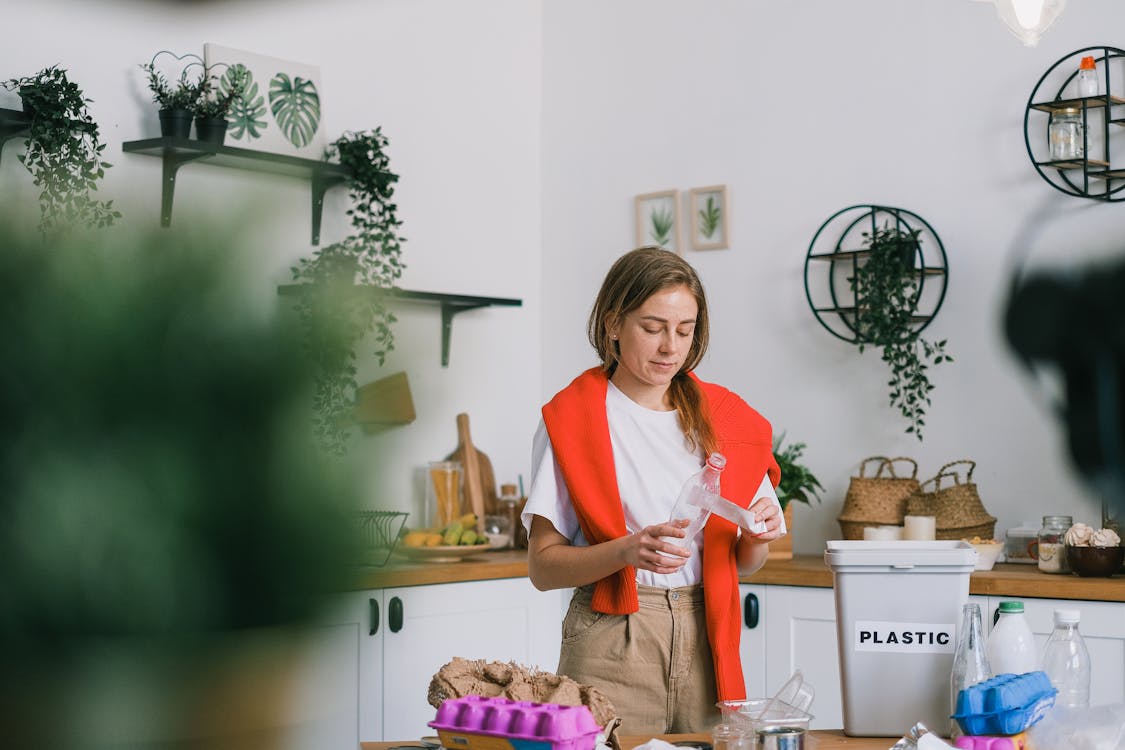 Free Calm woman in casual clothes standing near table and cleaning plastic bottle while sorting rubbish in light kitchen in daytime Stock Photo