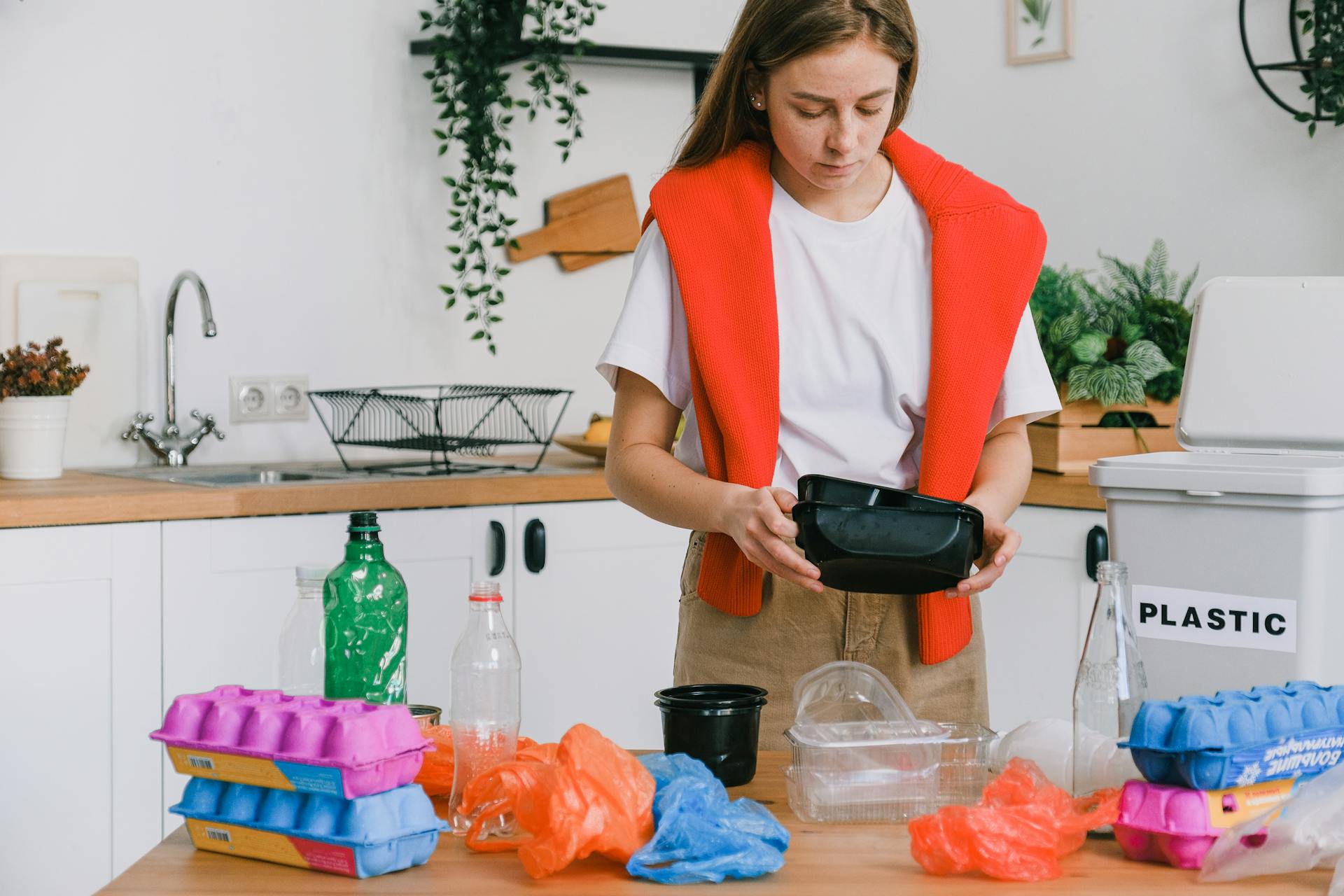 Eco friendly young female in casual clothes standing and sorting recyclable trash in light kitchen in daytime