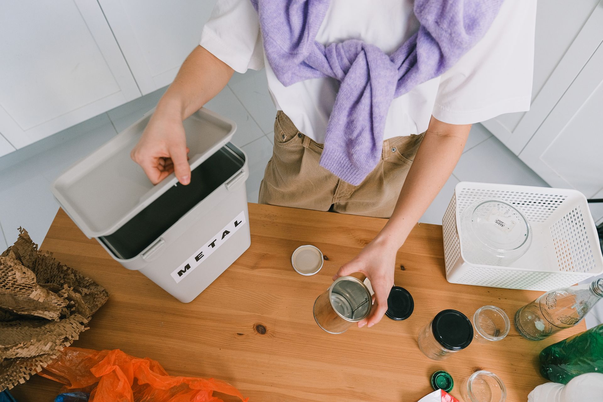 Person sorting metal waste in a kitchen for recycling. Eco-friendly home practice.