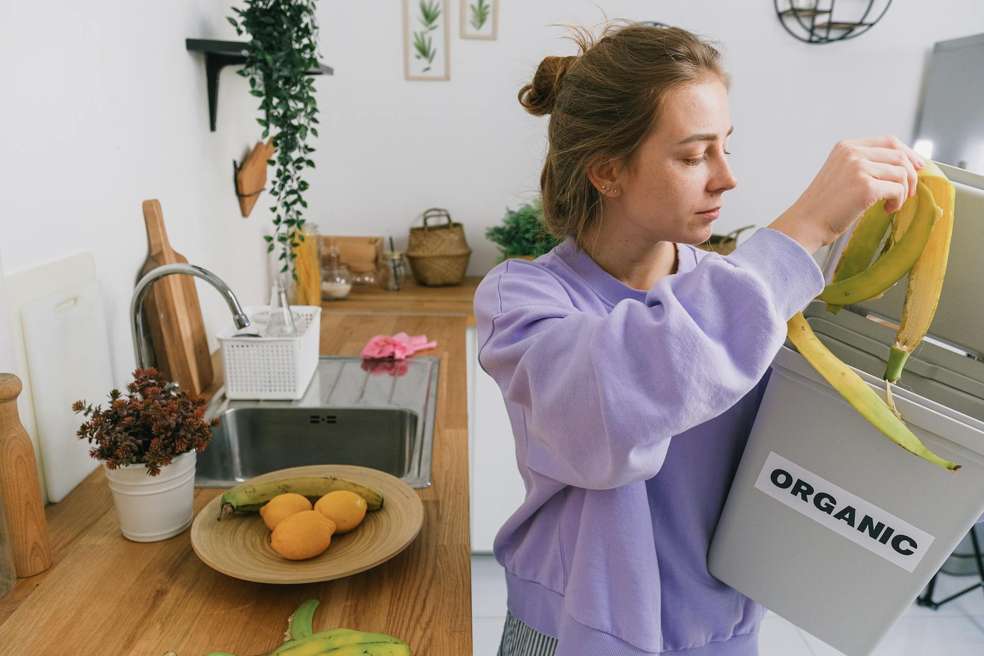A woman composts banana peels in an indoor organic bin, promoting sustainable living.
