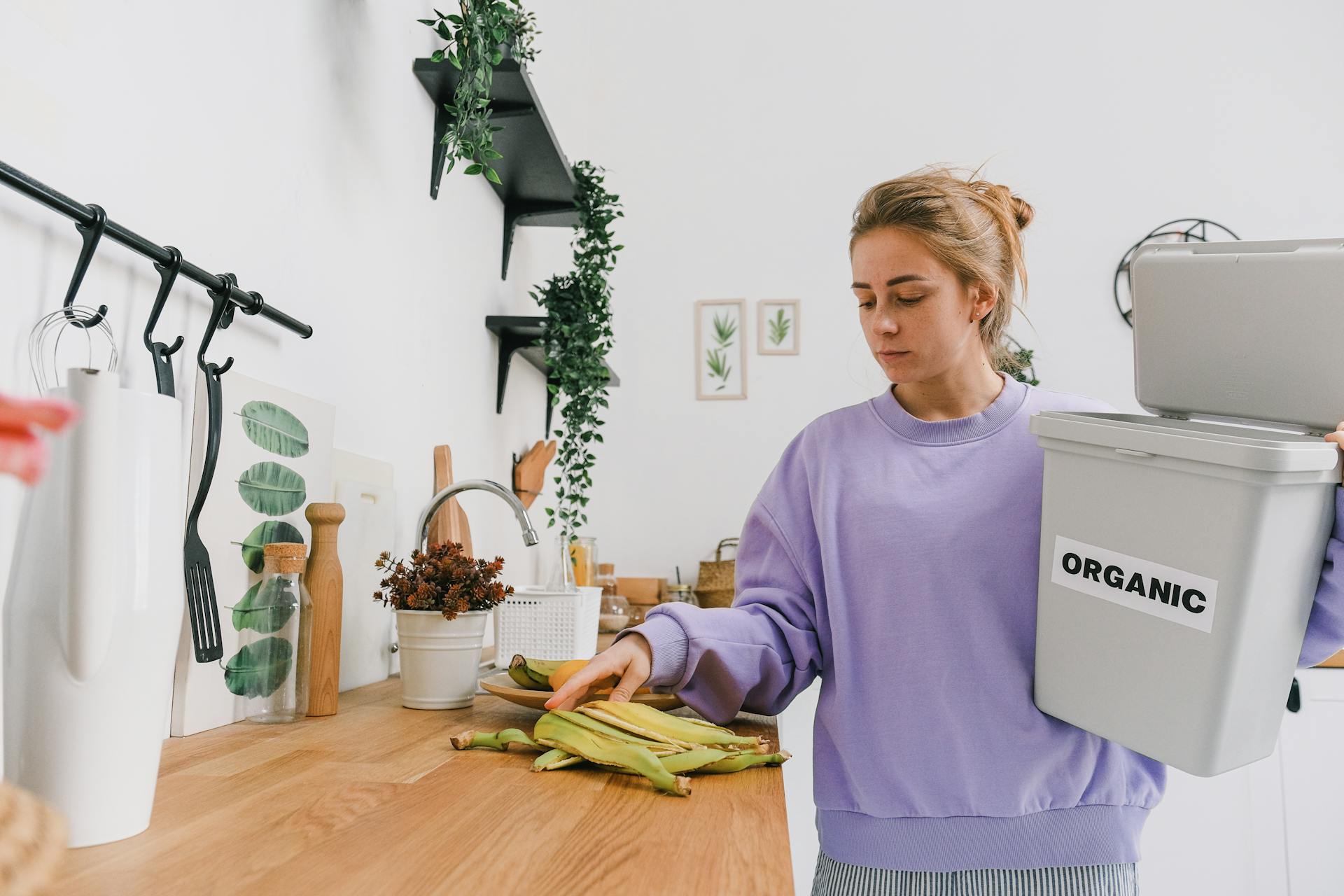 A young woman sorts organic waste in a clean, modern kitchen setting.