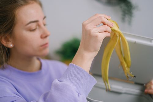 Free Close-up of a woman throwing a banana peel into a trash bin. Eco-friendly waste management. Stock Photo