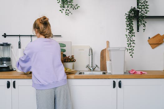 Young woman doing housework in a contemporary kitchen. Clean and tidy space with plants and kitchen equipment.