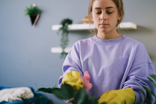 Young woman tending plants indoors, wearing yellow gloves, focused on gardening.
