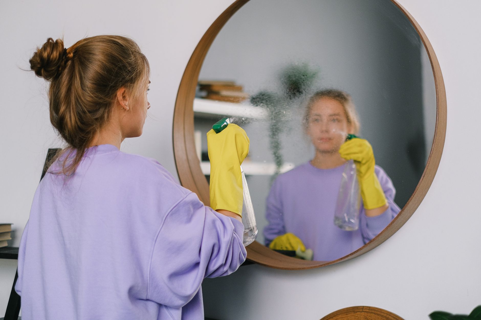 Woman using a spray bottle to clean a surface — swapping harsh cleaners is part of a skin-safe home environment audit