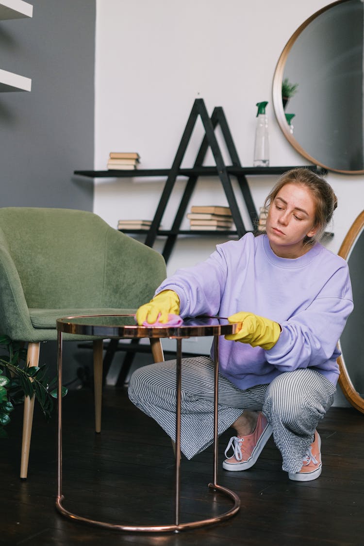 Female Squatting Down And Wiping Table In Light Room