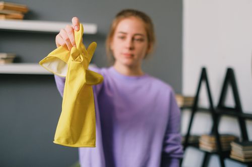 Free Calm blurred young woman in casual clothes reaching out hand with yellow latex gloves in light room in daytime Stock Photo