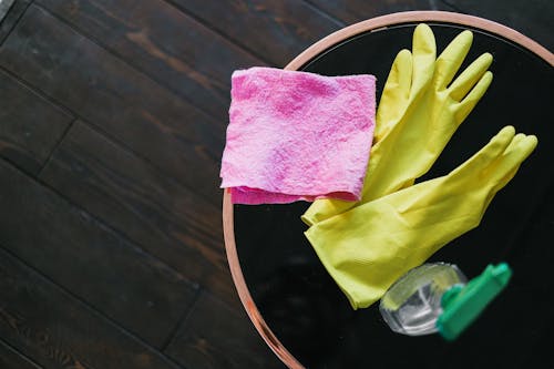Free Yellow gloves and pink cloth on a table with cleaner bottle, viewed from above. Stock Photo