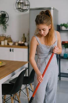A young woman mopping the floor in a stylish and modern kitchen setting.