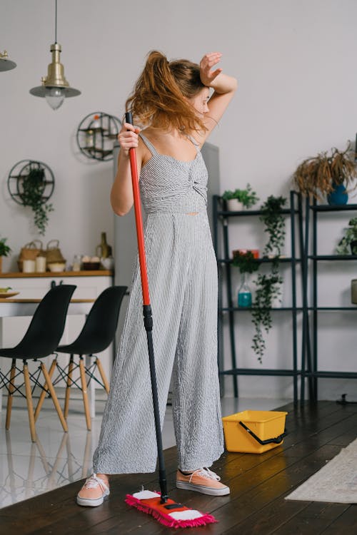 Tired housewife with mop during housework in room