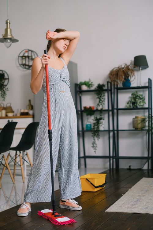 Free Exhausted young woman with mop and closed eyes wiping sweat from forehead after cleaning floor at home Stock Photo