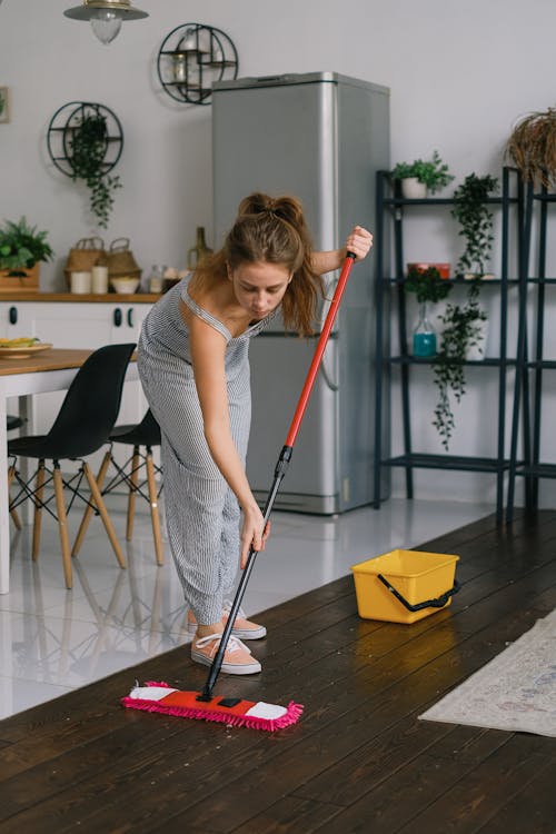 Young woman leaning forward while washing wooden floor with mop against kitchen at home in daytime