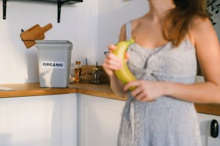 Crop woman with organic banana in hands standing in kitchen