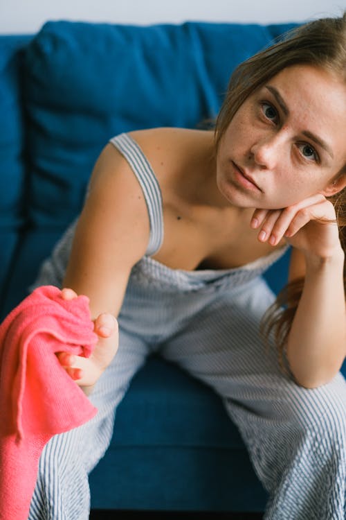 Free Crop upset young female in casual clothes with dusting cloth in hand sitting on cozy sofa in living room during household chores at home Stock Photo