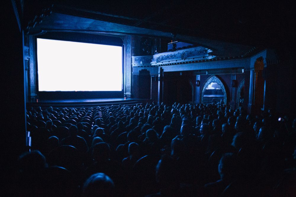 A full cinema auditorium, audience seated in front of a lit screen