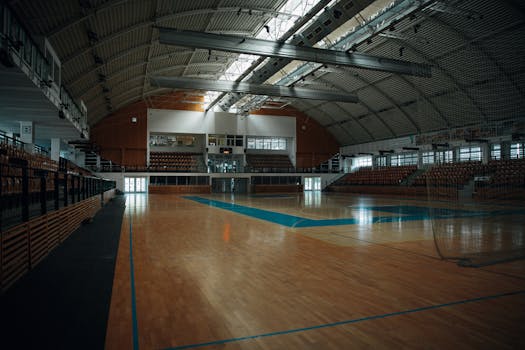 Empty indoor sports arena with hardwood flooring and bleachers, perfect for various sports activities.