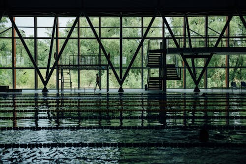 Anonymous sportsman silhouette strolling between rippled swimming pool and decorative wall against stairs