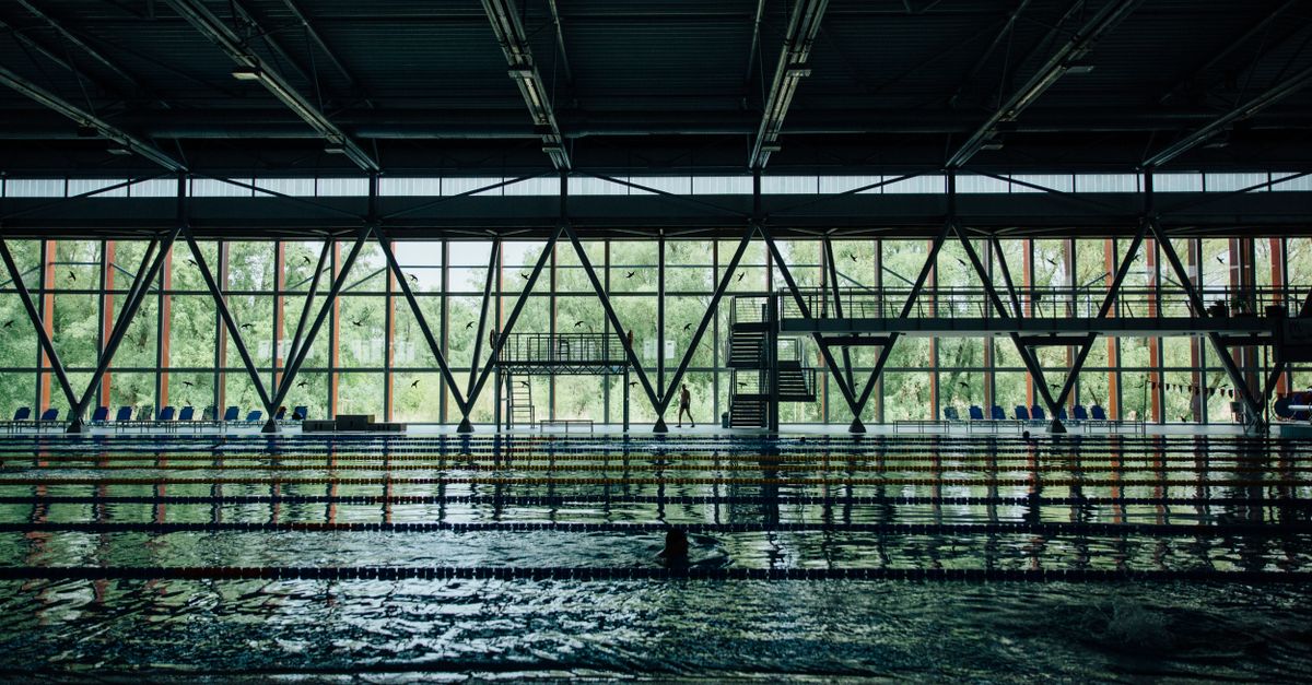 Unrecognizable sportsman silhouette strolling between decorative wall and swimming pool with rippled water and floating markers