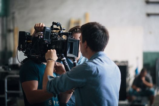 A film crew adjusting a video camera on an indoor set, focusing on technical preparation and teamwork.