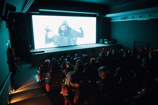 Crowded cinema theater with audience watching a movie on a large screen in a dark setting.