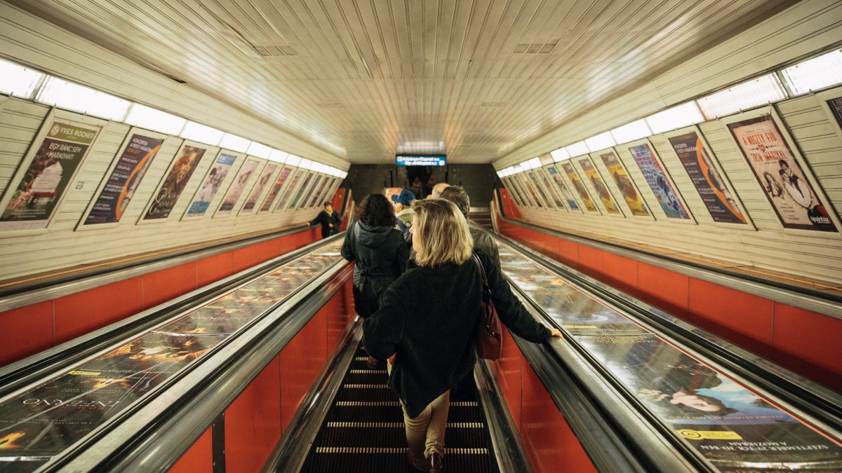 Commuters on an escalator in a Budapest metro station, Hungary, featuring vibrant posters.