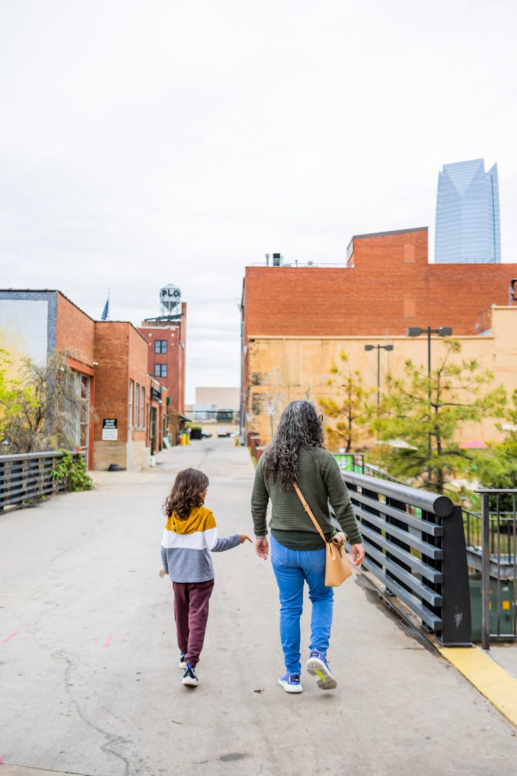 Grandmother With Granddaughter Walking On Bridge In Town