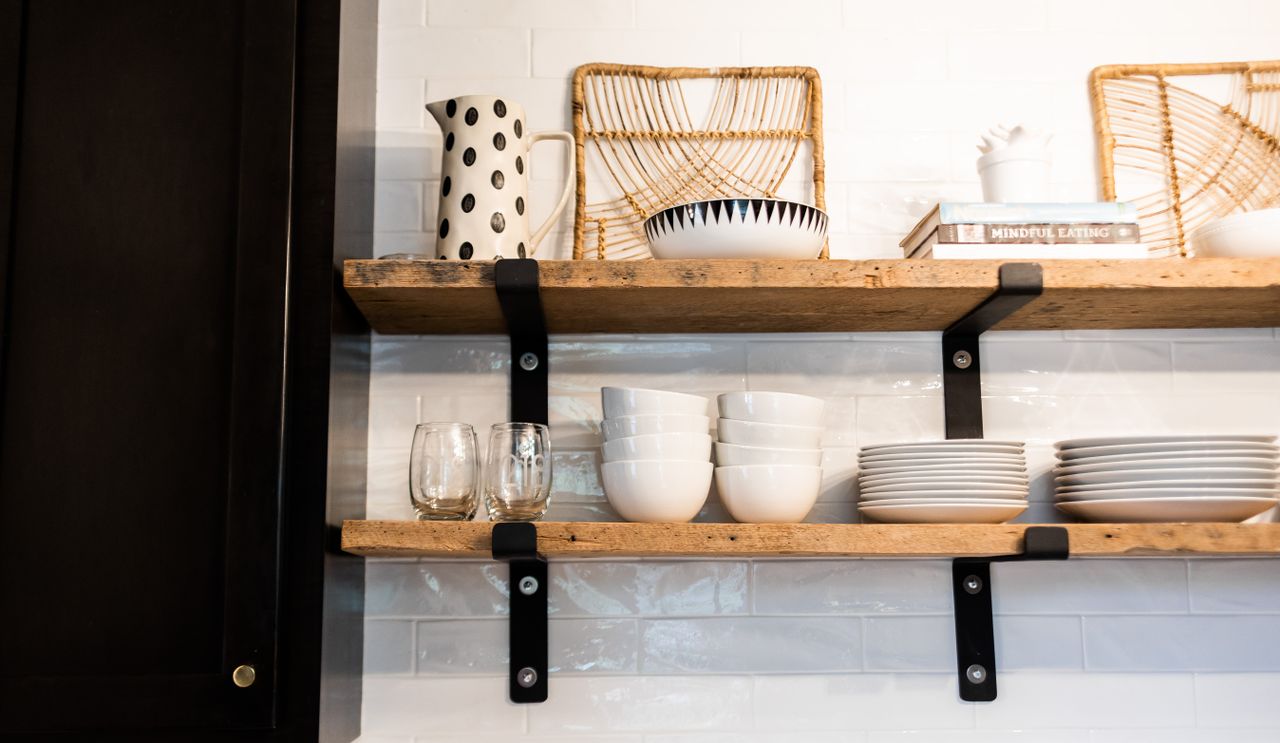 Rustic wooden open shelves holding stacks of white bowls, plates, and glasses