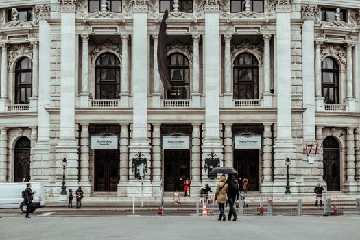 A detailed view of a grand historic building facade with pedestrians walking in front, showcasing architectural elegance.