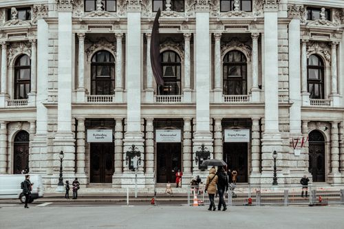 Free A detailed view of a grand historic building facade with pedestrians walking in front, showcasing architectural elegance. Stock Photo