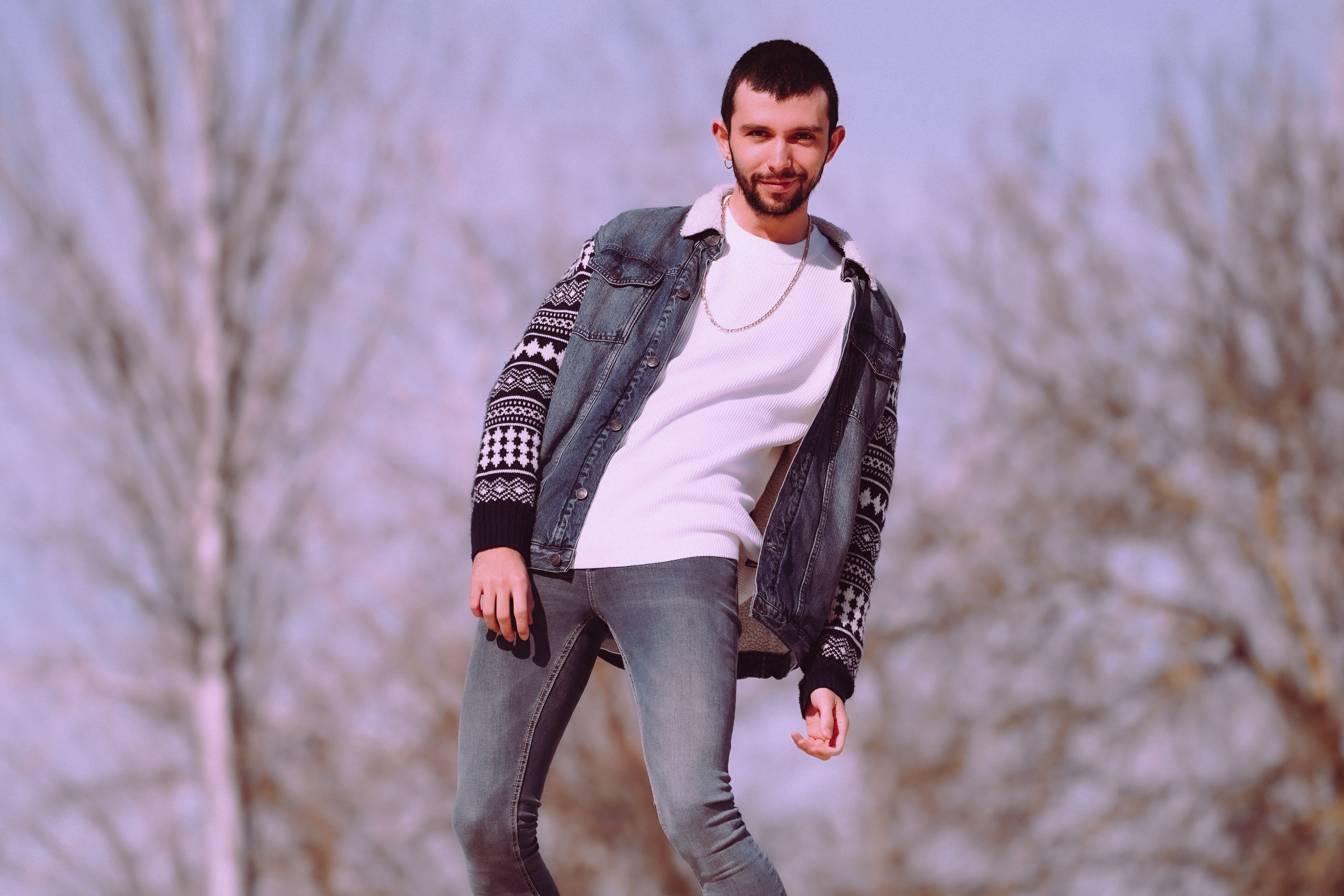 Homme en pull blanc superposé sous veste denim, look casual streetwear outdoor