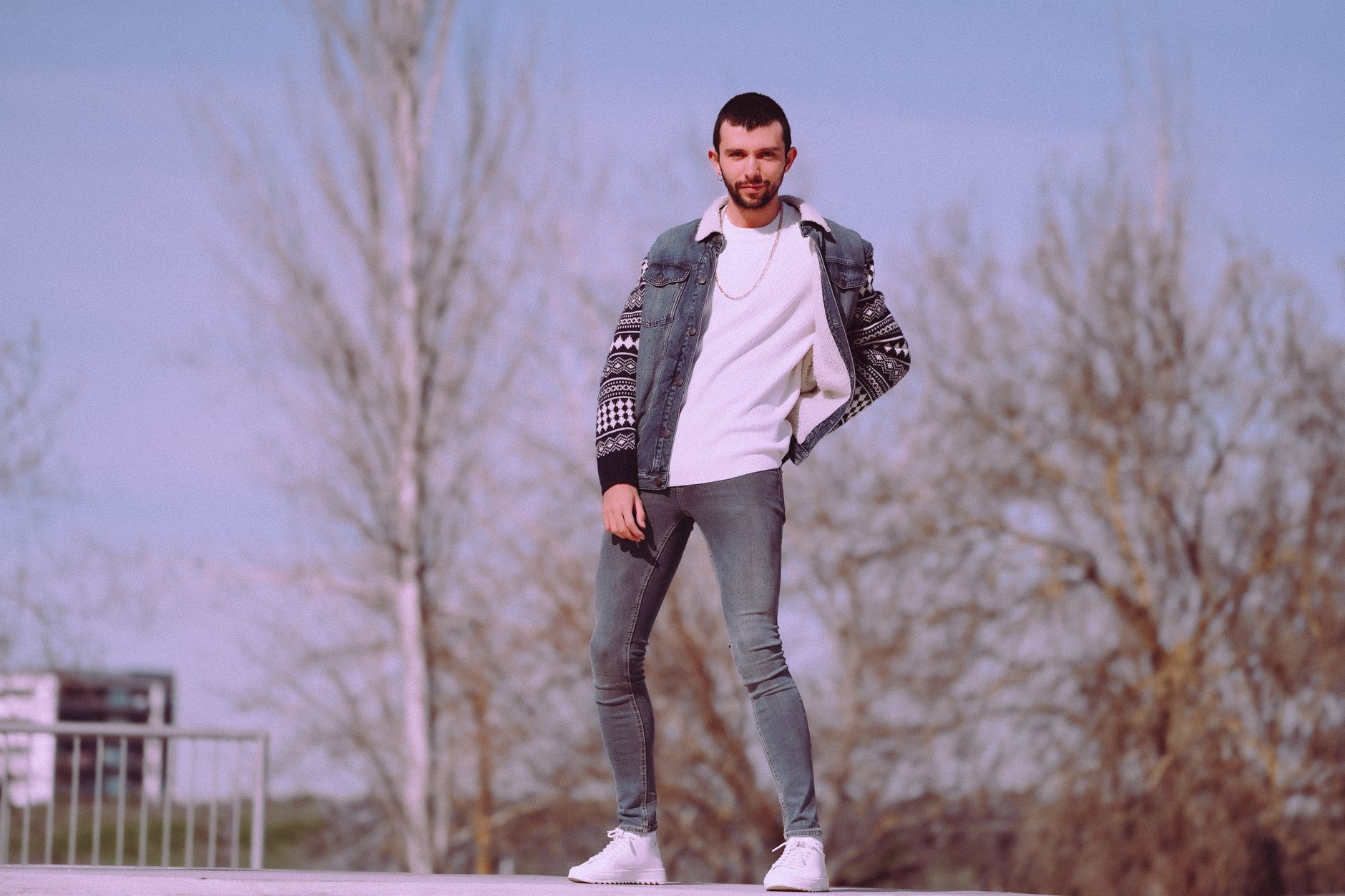 Fashionable man in denim and sneakers posing confidently outdoors.