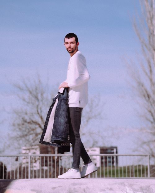 Free Man holding denim jacket in an urban area, showcasing modern fashion style on a sunny day. Stock Photo