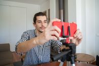 Confident young man adjusting smartphone on tripod for home vlogging setup.