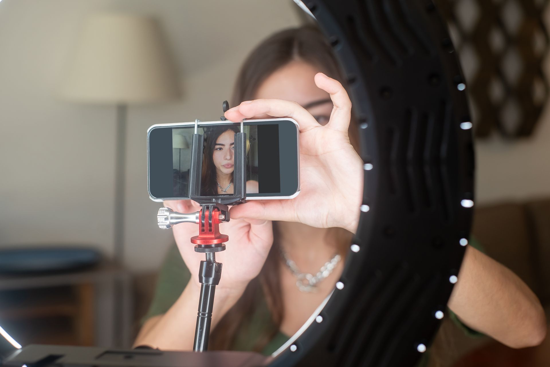 A young woman uses a smartphone with a ring light for online streaming at home.