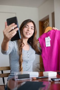 Young woman live streaming a fashion review while showcasing a pink dress from home.