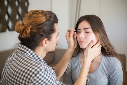 A makeup artist applies eye makeup to a woman indoors. Capturing beauty and artistry in a personal setting.