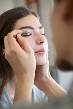 Close-up of a makeup artist applying eyeshadow to a woman's closed eyes.